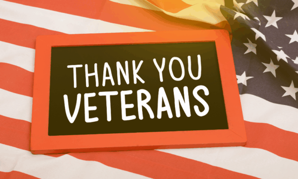 A small chalkboard with a red frame displays the message “Thank You Veterans” in white letters, resting on a gently folded American flag with stars and stripes.